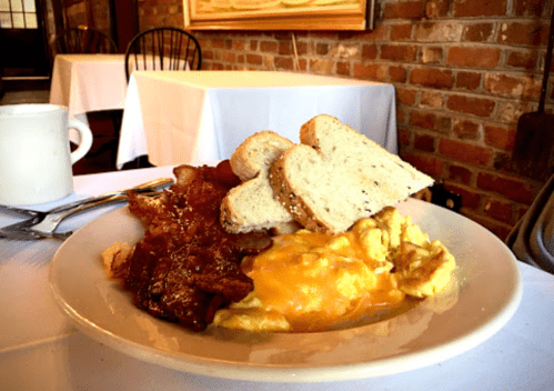 A plate of breakfast featuring scrambled eggs, bacon, and slices of whole grain toast on a table.