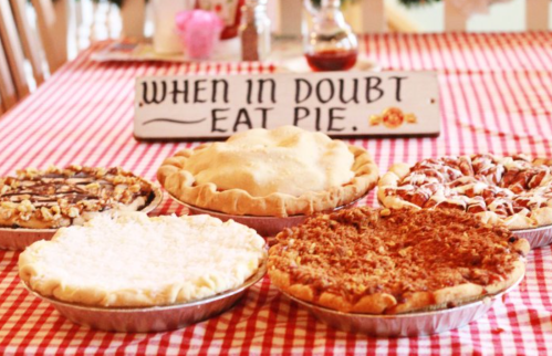 A table with five delicious pies and a sign that says, "When in doubt, eat pie," on a red and white checkered tablecloth.