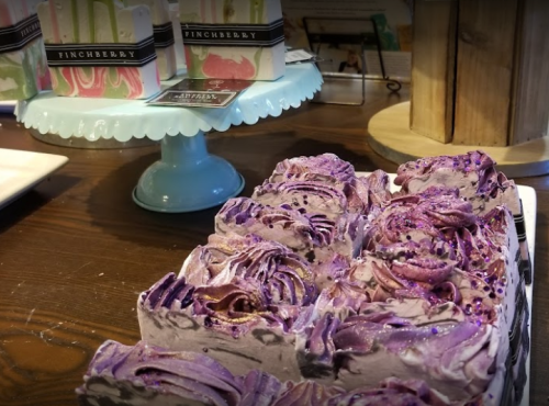 A close-up of a beautifully decorated purple soap with swirls and glitter, displayed alongside colorful soap bars.