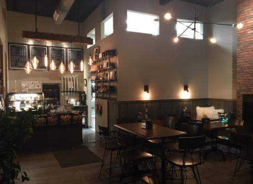 Cozy café interior with wooden tables, pendant lights, and a counter displaying menu items and snacks.