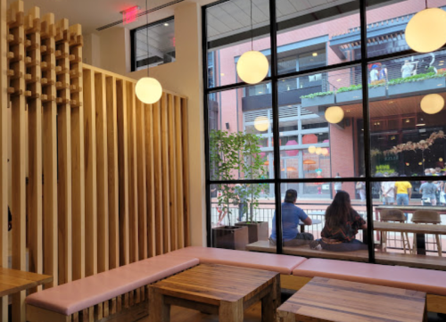 A cozy café interior with wooden seating, large windows, and patrons enjoying the view outside.