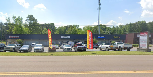 A row of businesses with colorful banners for "Breakfast" and "Lunch," parked cars, and a clear blue sky.