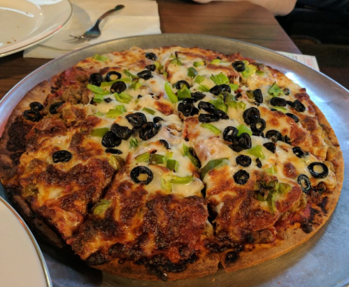 A freshly baked pizza topped with cheese, black olives, and green peppers, sliced and served on a metal tray.