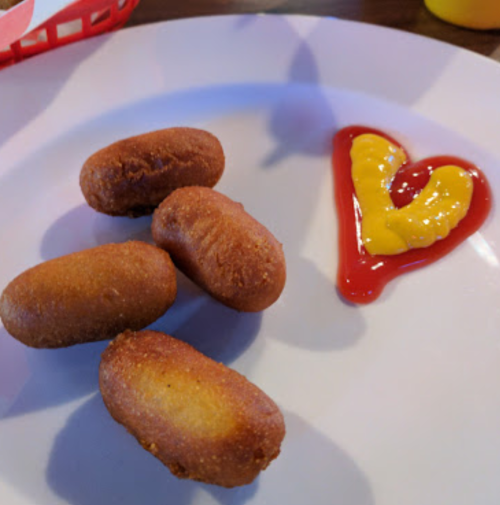 A plate with four golden-brown corn dogs and a heart-shaped design made of ketchup and mustard.