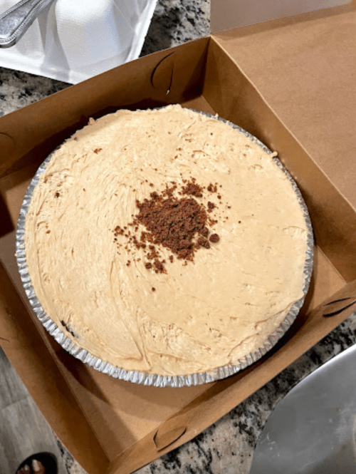 A creamy pie in a cardboard box, topped with a sprinkle of cocoa powder.