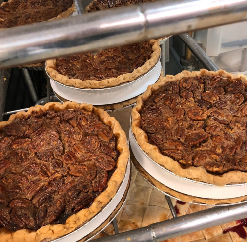 Four freshly baked pecan pies cooling on a metal rack, showcasing their golden crusts and rich, nutty filling.