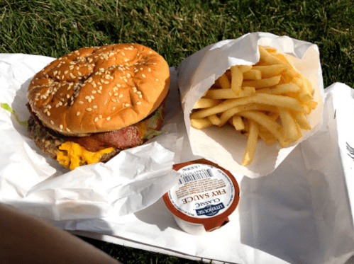 A sesame seed burger with cheese and bacon, accompanied by a side of fries and a small container of fry sauce.