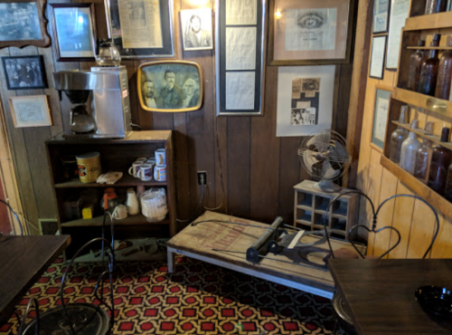 A cozy corner with vintage decor, including a coffee maker, framed photos, and a wooden bench against a wooden wall.