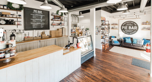A cozy pie bar interior featuring a wooden counter, display case, and seating area with decor and pie-themed signage.