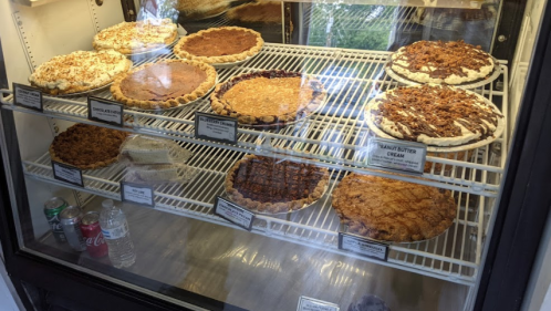 A display case filled with various pies, including pecan, pumpkin, and peanut butter cream, alongside drinks.