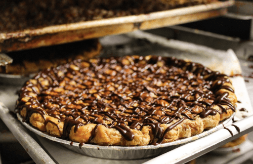 A freshly baked pie with a golden crust, topped with chocolate drizzle and nuts, sitting on a baking tray.