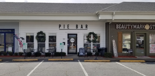 Exterior view of a storefront labeled "PIE BAR," featuring outdoor seating and holiday wreaths, next to a beauty store.