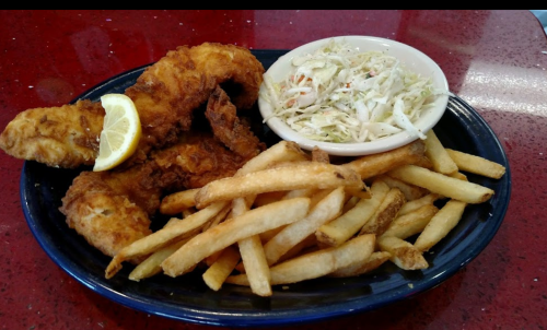 A plate of fried fish with a lemon wedge, served with coleslaw and a side of golden French fries.