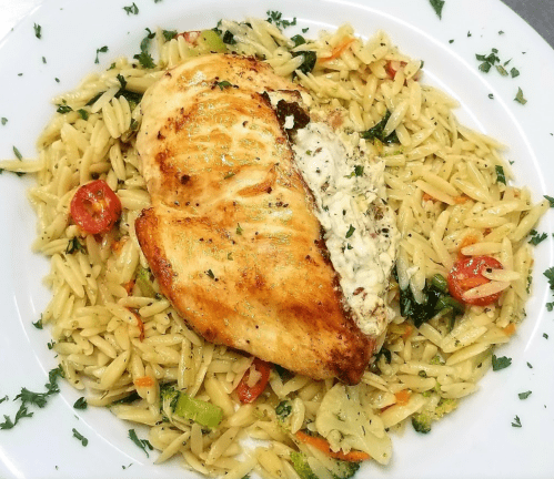 Grilled chicken breast stuffed with creamy filling, served on a bed of orzo pasta with mixed vegetables and herbs.