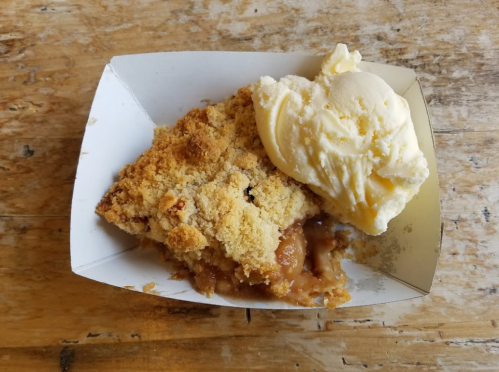 A serving of apple crumble topped with a scoop of vanilla ice cream on a wooden surface.