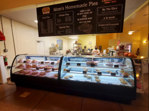 Display case filled with various homemade pies and cookies, with a menu board above in a cozy bakery setting.