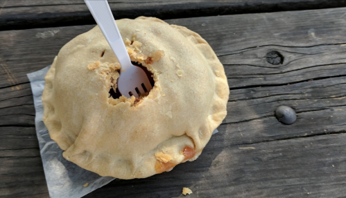 A baked pie with a fork inserted, resting on a wooden surface.