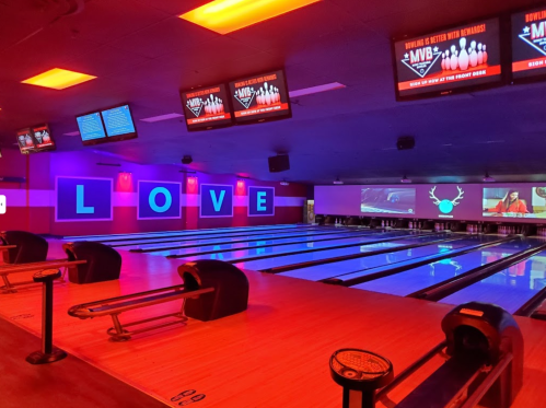 A vibrant bowling alley with neon lights spelling "LOVE" and multiple screens displaying scores and graphics.