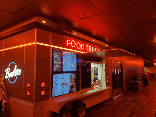 A brightly lit food truck with a menu display, set in a cozy indoor space with warm lighting.