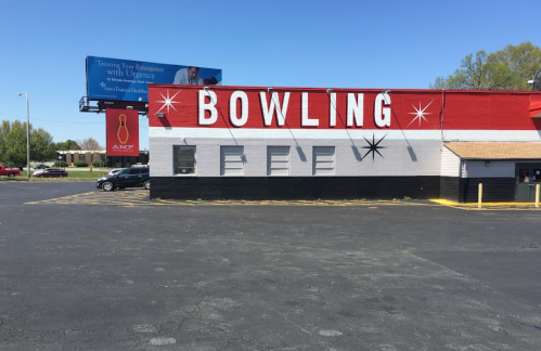 A bright red and white bowling alley building with large "BOWLING" letters on the side, set against a clear blue sky.