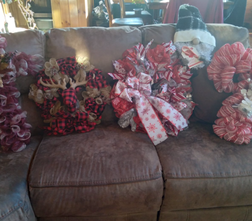A cozy couch displaying four decorative wreaths in various colors and styles, featuring bows and festive designs.