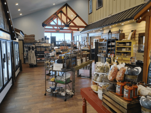 A bright, spacious store interior with shelves of products, a wooden ceiling, and large windows letting in natural light.