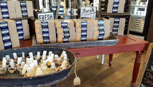 A display of boxed goods and tasting samples in a cozy shop, with signs indicating "Fresh" and "Fresh Baked."