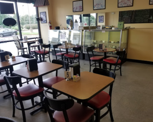 A cozy restaurant interior with empty tables, red chairs, and a display case in the background.