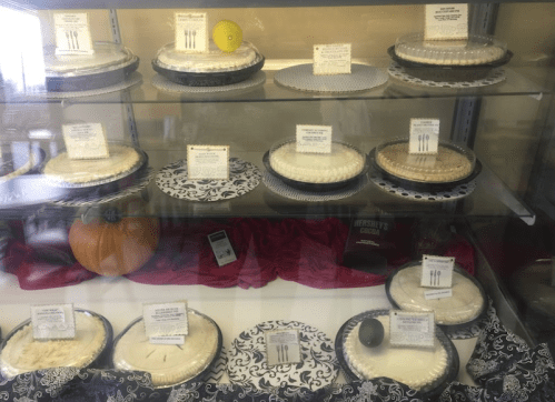 A display case filled with various pies, each labeled with descriptions, set against a decorative background.