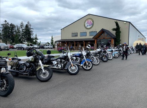 A row of motorcycles parked outside a large building with a grassy area and cloudy sky in the background.