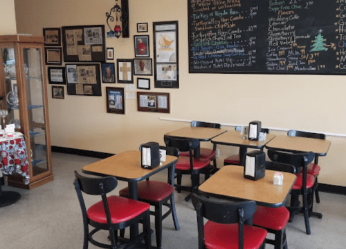 Cozy café interior with wooden tables, red chairs, and framed photos on the walls. A display case is visible.