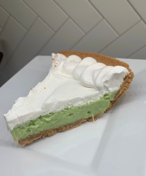 A slice of green pie with a graham cracker crust and whipped cream topping on a white plate.