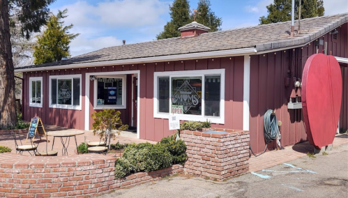 A charming red building with a sign reading "Open," surrounded by greenery and outdoor seating.