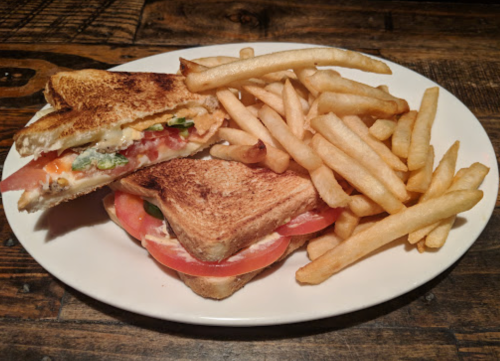 A toasted sandwich with tomatoes and lettuce, served with a side of golden French fries on a white plate.
