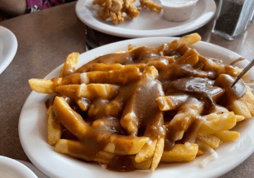 A plate of French fries topped with brown gravy and a drizzle of white sauce, served in a casual dining setting.