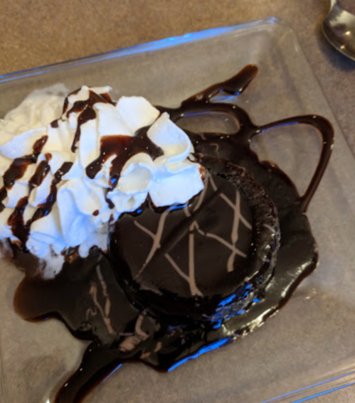 A chocolate dessert topped with whipped cream and drizzled with chocolate sauce on a clear plate.