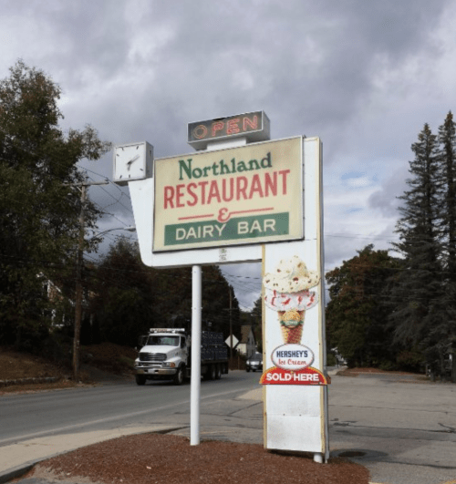 Sign for Northland Restaurant & Dairy Bar, featuring an ice cream advertisement, with a cloudy sky in the background.