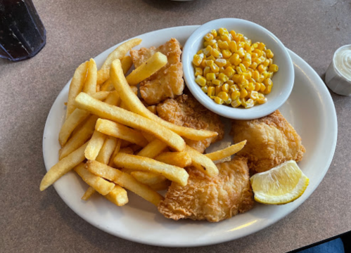 A plate of fried fish fillets, golden fries, a side of corn, and a lemon wedge.