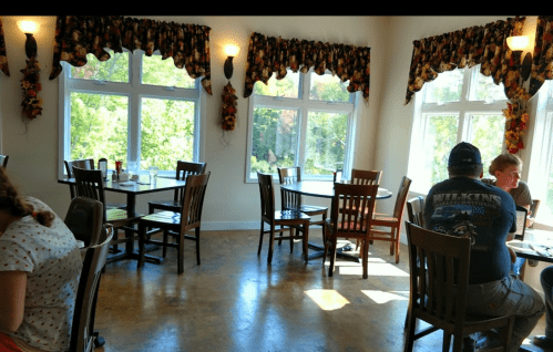 A bright restaurant interior with tables, chairs, and large windows, featuring diners enjoying their meals.