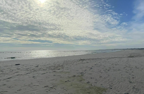 A serene beach scene with soft waves, a cloudy sky, and sunlight reflecting on the water.