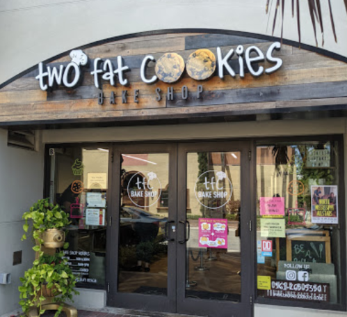Exterior of "Two Fat Cookies" bake shop with a wooden sign and colorful storefront decorations.
