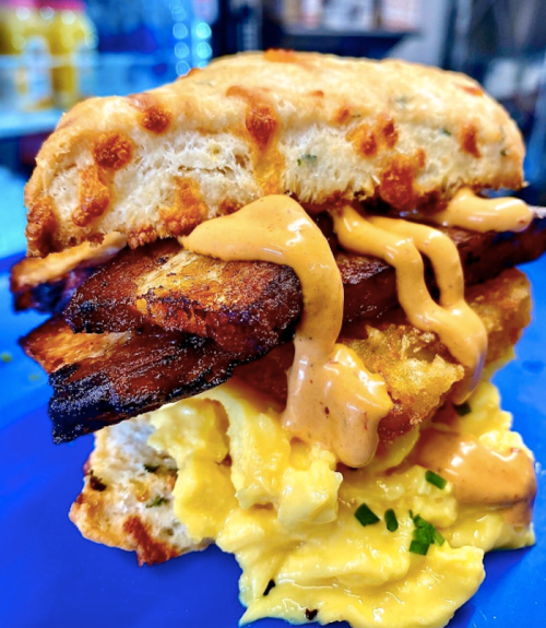 A close-up of a sandwich with crispy bacon, scrambled eggs, and a creamy sauce, all in a fluffy biscuit.