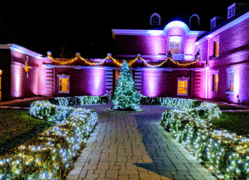 A beautifully lit courtyard at night, featuring a decorated tree and glowing pathways surrounded by colorful lights.
