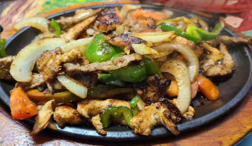 Sizzling fajitas with grilled chicken, bell peppers, onions, and tomatoes on a hot skillet.