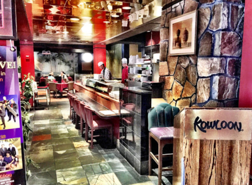 Interior of a restaurant featuring a stone wall, wooden accents, and chefs preparing food in an inviting atmosphere.