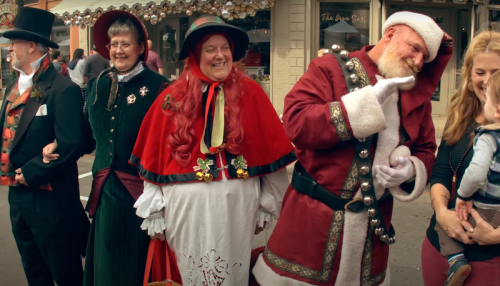 A group of people in festive costumes, including Santa, smiling and posing together during a holiday event.