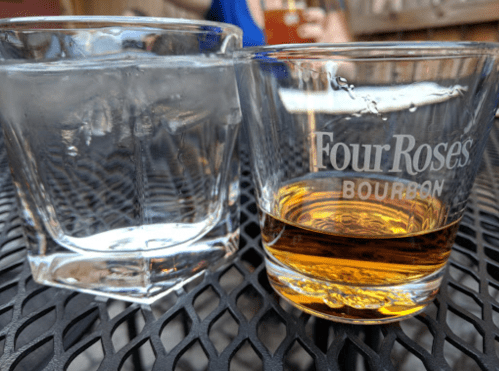 A glass of bourbon next to a glass of water on a textured black table.