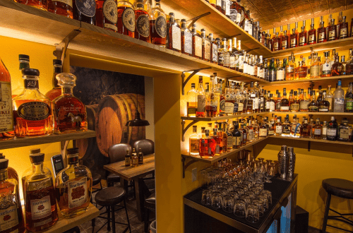 A cozy bar with shelves lined with various whiskey bottles and a wooden barrel in the background.