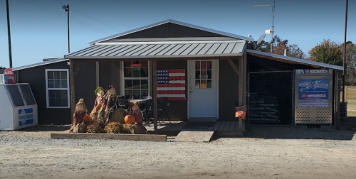 A rustic building with an American flag on the door, decorated with hay bales and pumpkins for fall.