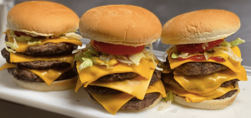 Three stacked cheeseburgers with lettuce, tomato, and ketchup on a white plate.